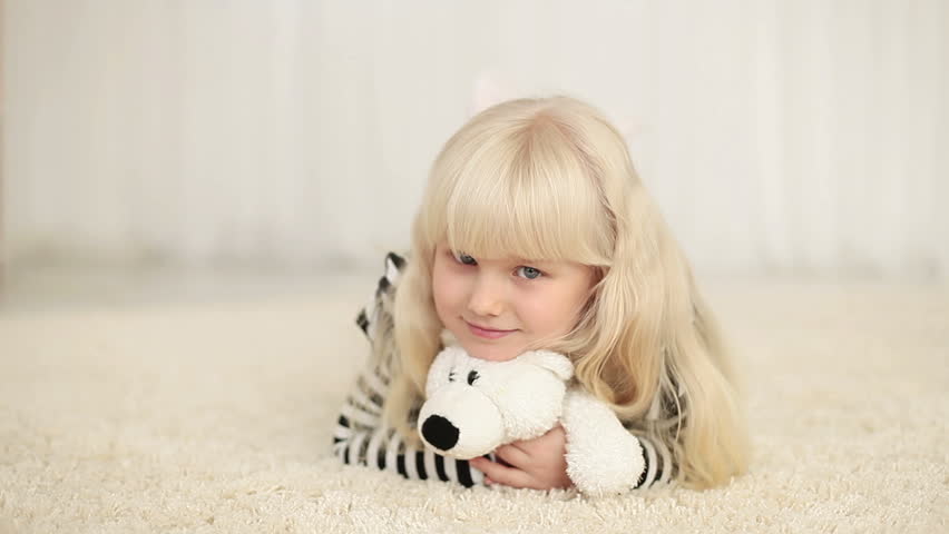 Happy little girl lying with teddy bear on the carpet 