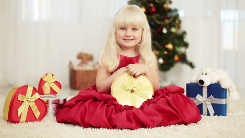Laughing baby is holding a gift beside Christmas tree, and sitting on the carpet