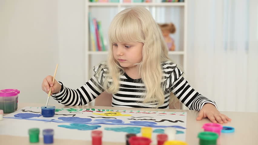 Little blonde girl paints pictures on a sheet of paper 