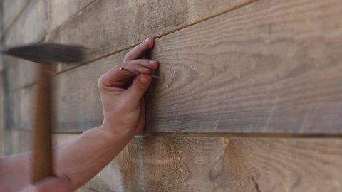 Nailing a nail into a wood board, close up. Detail of worker with a nail and a hammer. The handyman professionally hammers a nail into a woodboard with a hammer