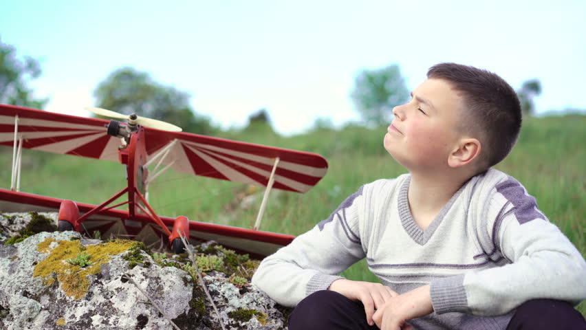 Close up boy  sitting near toy airplane on the stone and looking on the sky. 4k