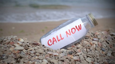 Call now written on paper as a message in a bottle washed ashore