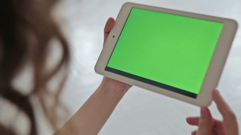 Back view of woman at home using electronic tablet, green screen