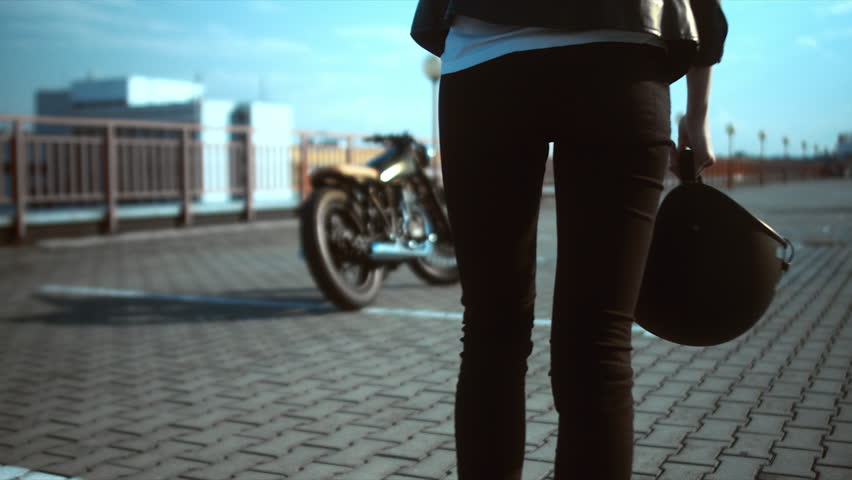 Young sexy Caucasian female biker walking towards her custom cafe racer motorcycle with helmet in hands. 60 FPS slow motion. Blackmagic URSA Mini