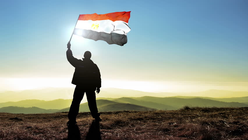 Successful silhouette man winner waving Egypt flag on top of the mountain peak, 4k cinemagraph