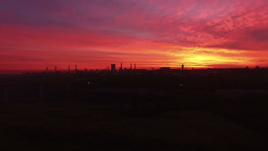 Aerial View over Industrialized City ringway bridge with air pollution from heat electric generation plant in apocalyptic red sunset scene.