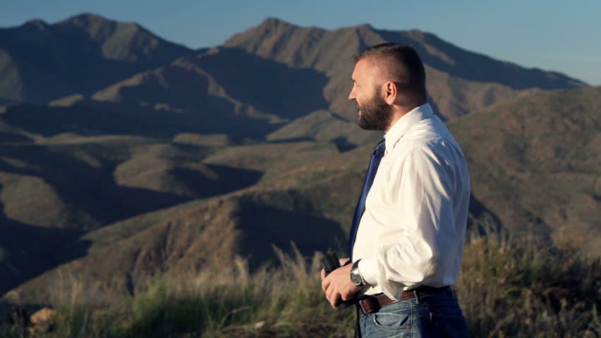 Young businessman looking at land through binoculars in country
