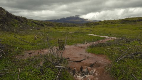 Time-lapse of muddy floodwater running down a gully from Cotopaxi Volcano, partially hidden in the mist. In the Andes, Ecuador.
