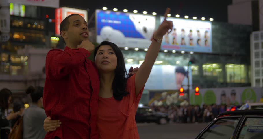 Mixed race couple visiting Tokyo, Japan sight seeing and pointing at Shibuya crossing Hachiko exit. Asian girlfriend and mixed-race boyfriend Romantic fun couple 