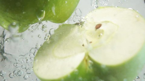 Two fresh green apple halves plunging into transparent water with stunning explosive splash breaking water surface on white background isolated. High-speed camera super slow motion shot. Underwater