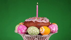 Easter cake with burning candle and eggs rotating in front of green background
