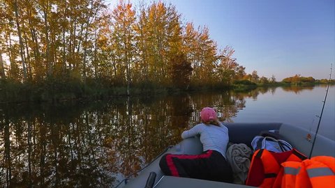 Rubber boat with fisher moving near riverside with yellow trees