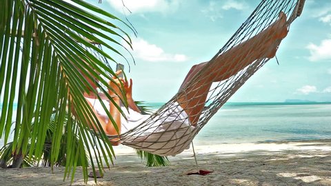 Young caucasian woman resting in a hammock with phone  on a tropical beach