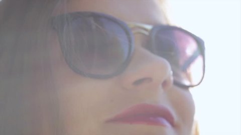 Beautiful girl in sunglasses with red lips enjoying the sunlight on nature. Sunlight creates iridescent reflections in the frame. Her sunglasses reflect trees and blue sky.
