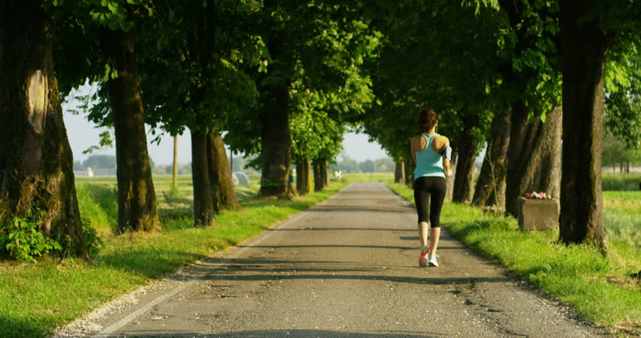 in a sunny spring day, a young girl goes to run under a tree-lined avenue to keep fit and for the welfare of his body while listening to music and is happy in slow motion 