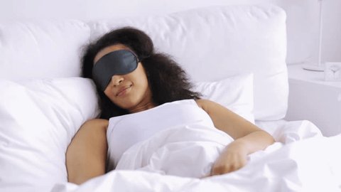 rest, comfort and people concept - young african woman in sleeping mask waking up in bed at home bedroom