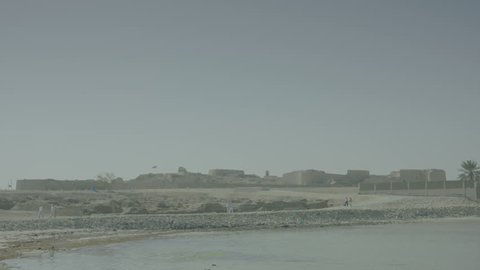 Bahrain - circa 2012 - Wide shot of Bahrain Fort seen from the sea. Visitors walk towards the site along the seashore. Tilt shift lens used to create a special effect by playing with depths of field.