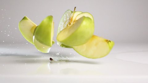 Fresh tasty green apple falling down and breaking up into pieces and rolling onto it sides on wet white floor with stunning explosive splash. Shoot with high speed camera in slow motion mode. White