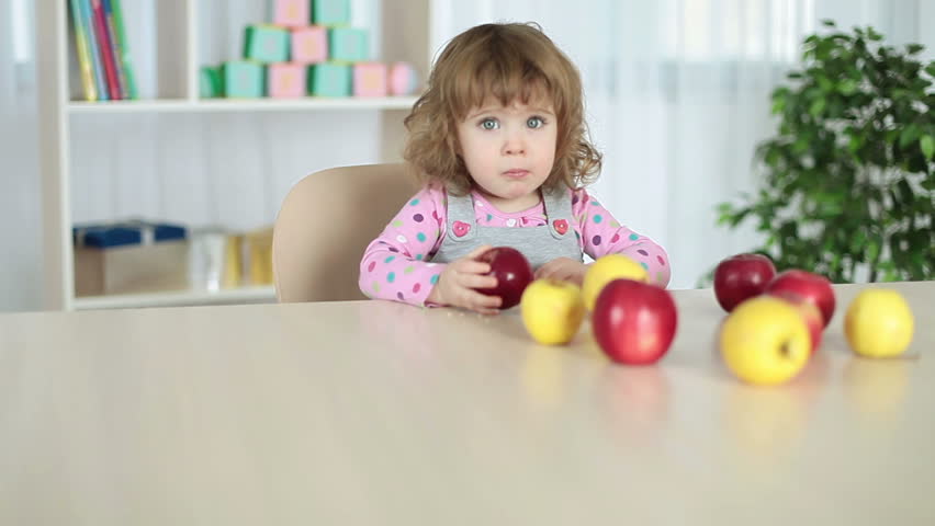 Baby girl eats apples sitting at the table 