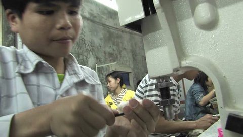 CHINA - CIRCA 2009: A child trying to fix a sewing machine with the help of a wench in a sweatshop in China circa 2009