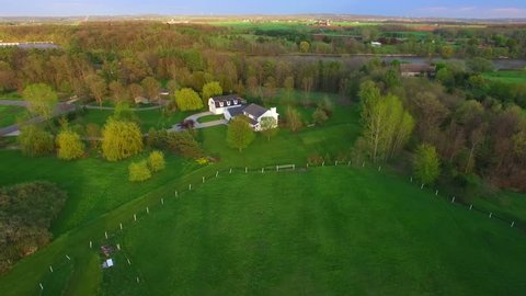 Evening aerial flyby of large rural home with many trees in Springtime.
