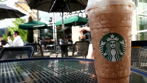 Coquitlam, BC, Canada - May 04, 2016 : One side of people drinking Starbucks coffee on sunny day, focus on ice frappuccino