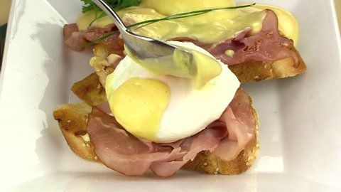 Placing hollandaise sauce on poached eggs on ham on toast for eggs benedict.

