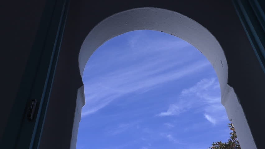 View of white bird flying in the blue sky through arch window from dark room, symbol of freedom