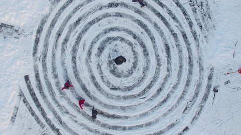 Parents and children slide by icy pond with spirals near name Ann on snow at winter day. Aerial view