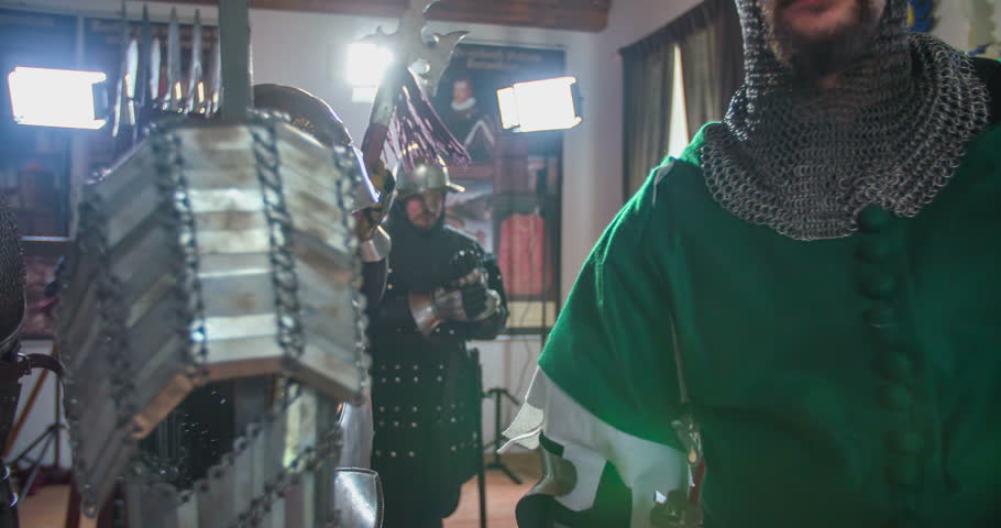 Knights are leaving the room in order to go to a battle. They are fully dressed and are taking helmets, swords and spears. Close-up shot.