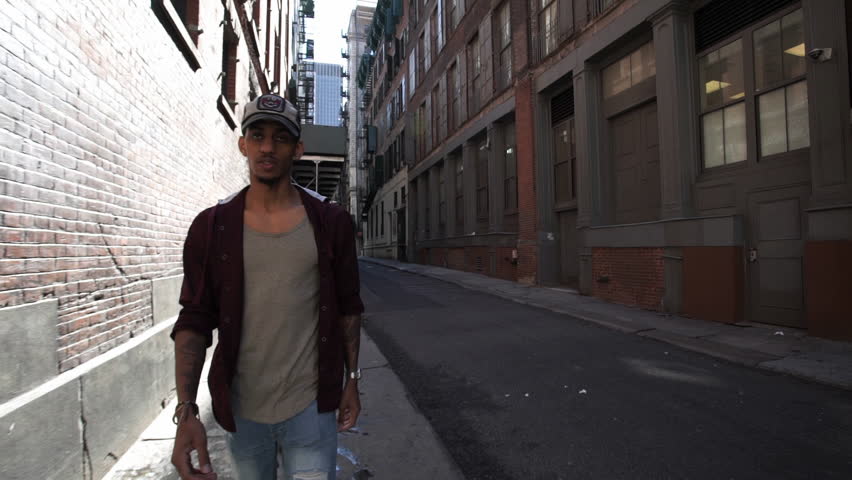 A young, athletic, black man walks through a sun filled alley. New York, NY - March, 2016