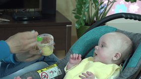 Mother feeding baby food to baby. The kid is eating with appetite. Mother put potato mash in infant child mouth at home. Zoom out shot. 4K UHD video clip.