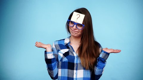 Woman confused thinking seeks a solution, paper card with question mark on her head. Doubtful young female studio shot blue background. 4K ProRes HQ codec