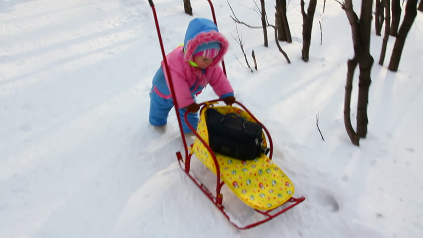 baby girl pushes sled in winter park