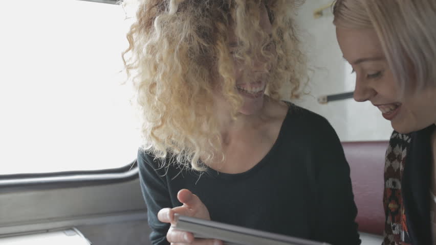 Smiling girlfriends using tablet PC in trip by train
