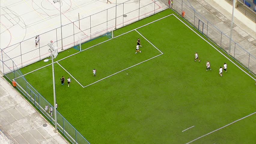 Aerial of sports field people playing football in favela, zooms out to coast view of Rio de Janeiro, Brazil