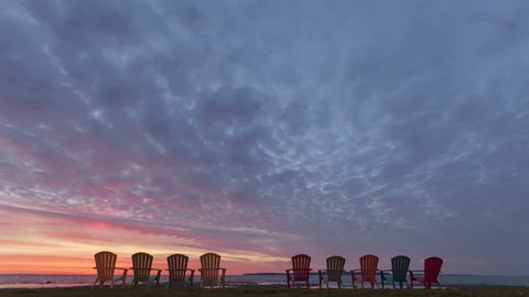 4K Time lapse of a sunrise behind a row of chairs at lake Huron in Michigan, USA with colored clouds