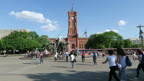 BERLIN, BERLIN/ GERMANY MAY 09 2016: People walking across the Alexanderplatz with its Neptune fountain and the town hall rotes rathaus in Berlin. Camera pan to tv tower.