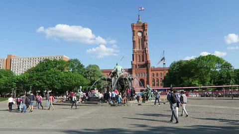 BERLIN, BERLIN/ GERMANY MAY 09 2016: People walking across the Alexanderplatz with its Neptune fountain and the town hall rotes rathaus in Berlin. Camera pan to tv tower.