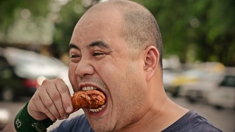 Fat Asian bald head Thai man is biting and eating fried chicken drumstick greedily with hunger with water sweat on his face in HD (best quality)