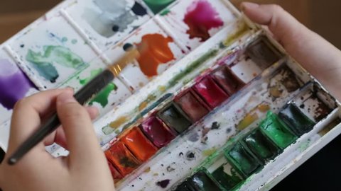 Girl stirs watercolor paints with water on a palette. Filmed with rig