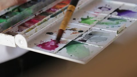 Girl stirs watercolor paints with water on a palette. Filmed with rig