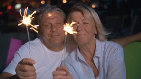 Slow motion clip of a nice senior couple with lit sparklers outdoors at night. They are very gentle to each other, looking in love and happy 
