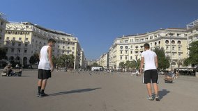 Slow motion steadicam clip of two young men doing acrobatic tricks on city square. Scene with people going by, taking pictures of them and flying pigeons