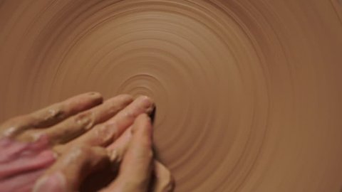 Hands working on a potter's wheel , making a relief on a clay plate