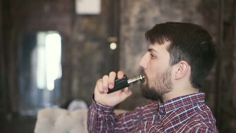 Handsome young man smoking electric e cigarette vapor indoors