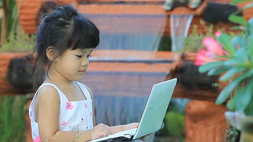Little girl with a small portable computer in the home garden.