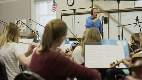 Medium panning shot of conductor leading school orchestra / American Fork, Utah, United States