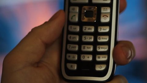 a male hand holds up a phone and types a number, in the background is some colorful animation 