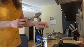 Man holding baby take banana fruit from refrigerator and woman mixing soup food in steamy pot. Young family together in kitchen. Static shot. 4K UHD video clip.